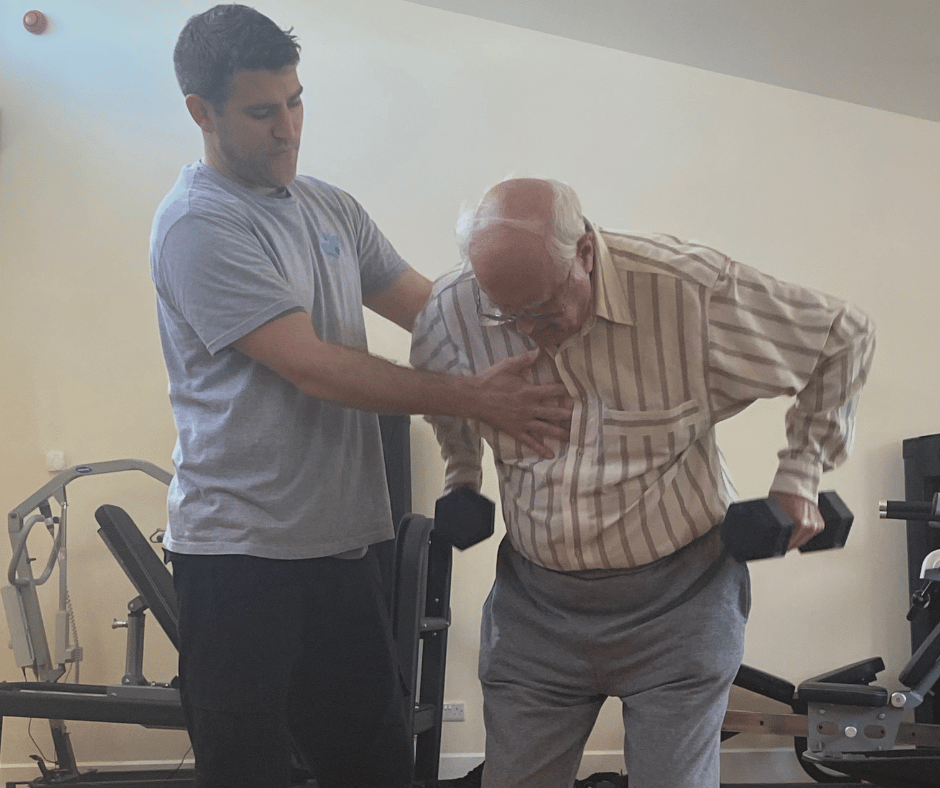 Image of Alan using hand weights whilst supported by physio Tom