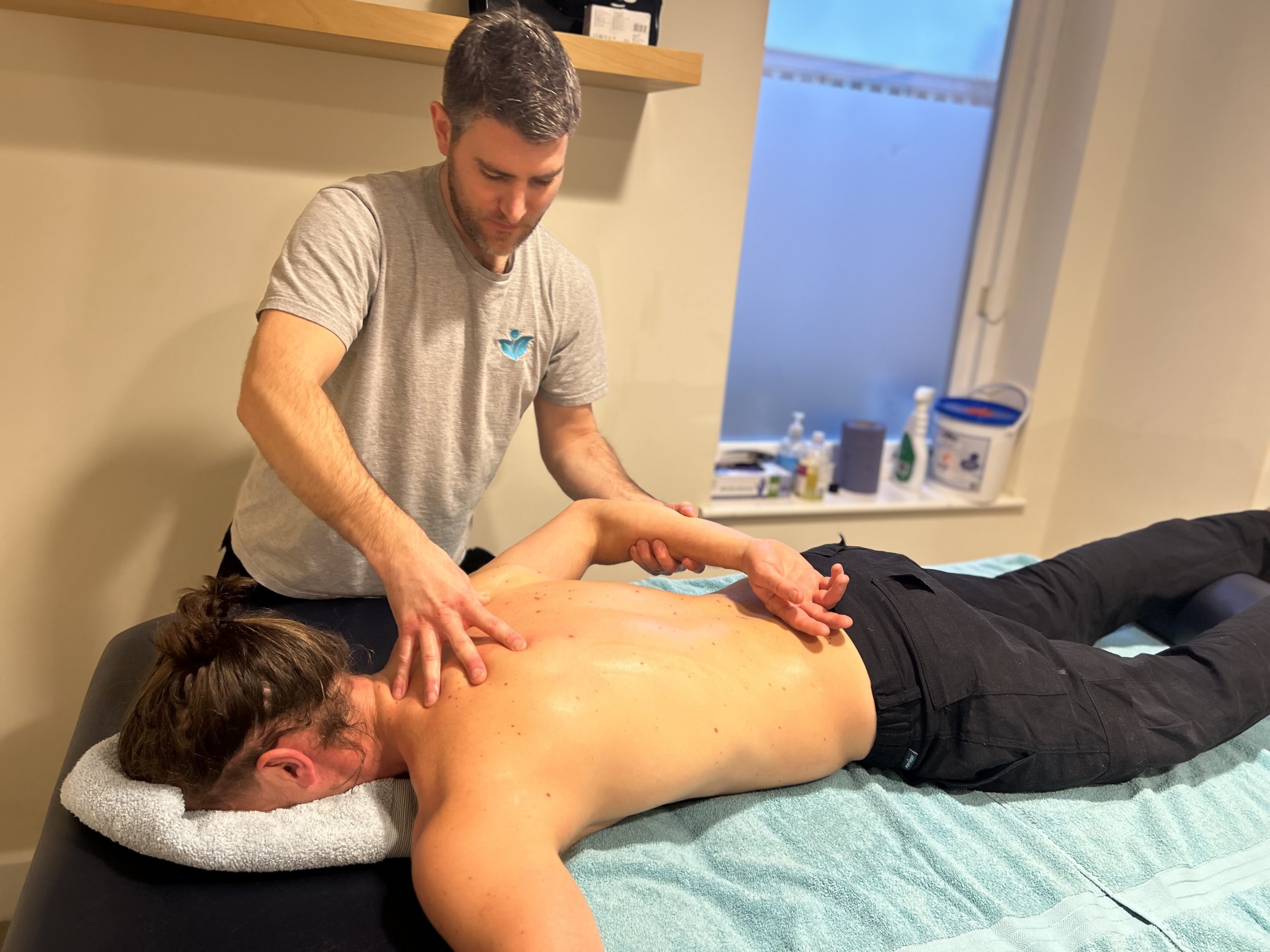 a man is laying face down on a massage bed whilst sports therapist Tom massages his back