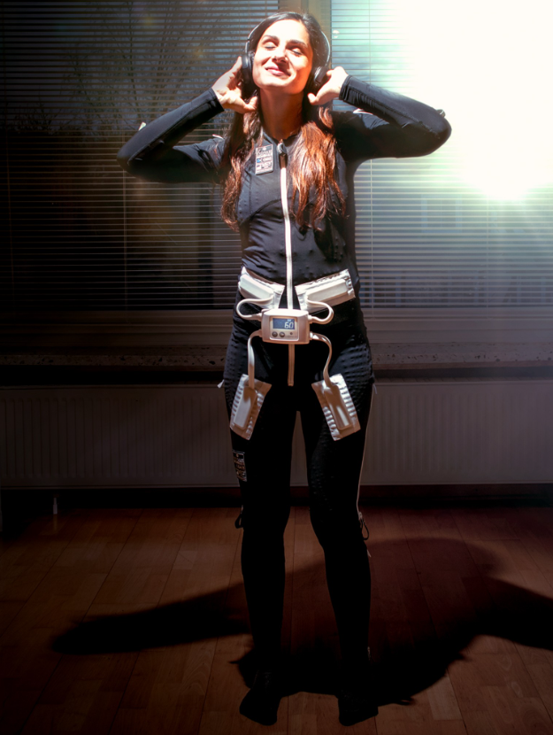 a full body shot of a woman wearing the black mollii suit and head phones she is smiling looking up to the sky.