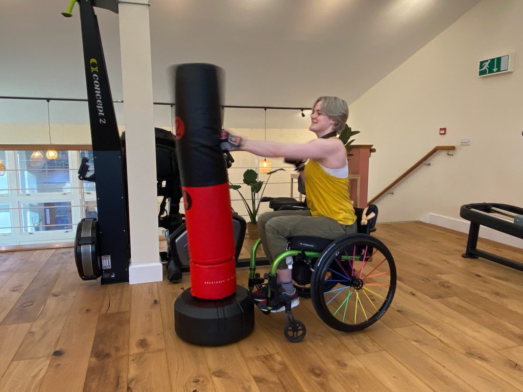 woman with FND sat in her wheel chair whilst using boxing pillar