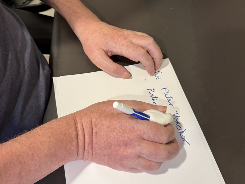close up of the hands of someone using a mold to grip a pen and write their name in an occupational therapy session